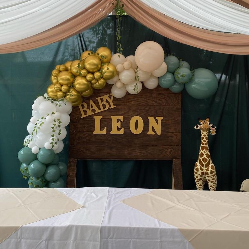 Gold, cream, white and sage balloon garland over a wooden “Baby Leon” sign