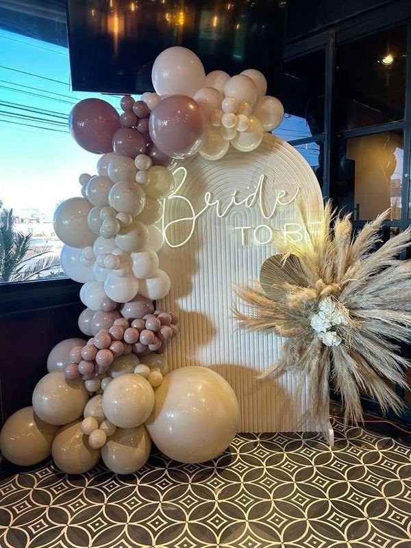 Neutral, nude and mauve balloon garland around a “Bride to Be” neon arch with pampas grass