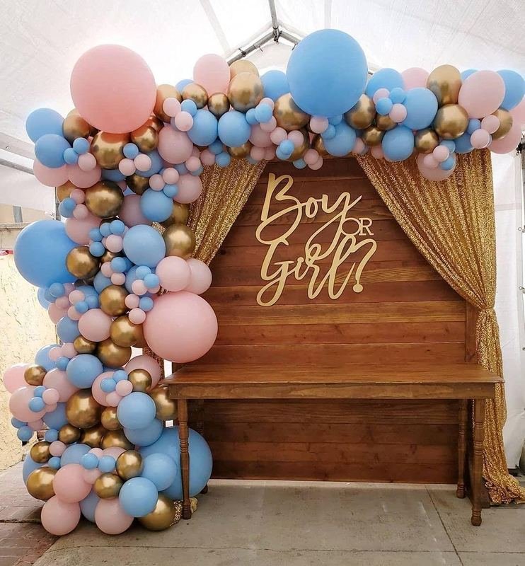 Pink, blue and gold balloon garland framing a “Boy or Girl?” gender reveal backdrop