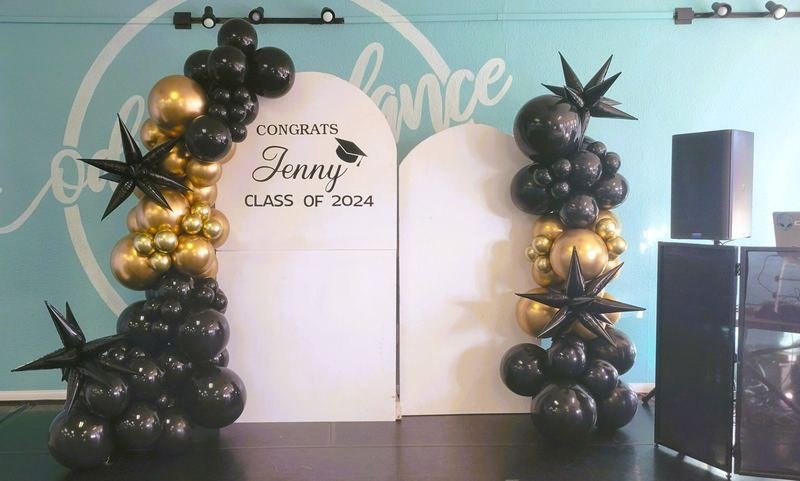 Black and gold balloon columns with star balloons beside a “Congrats Jenny, Class of 2024” graduation backdrop
