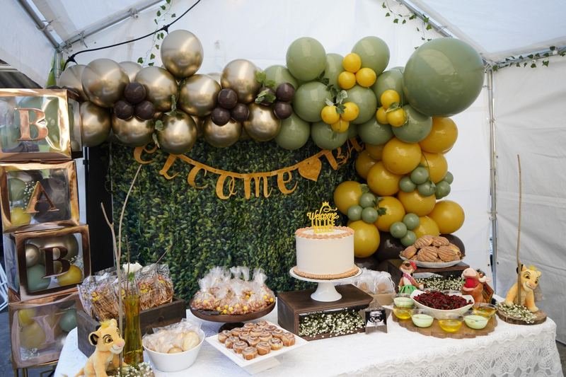 Sage green, gold and mustard balloon garland over a “Welcome Little King” baby shower dessert table